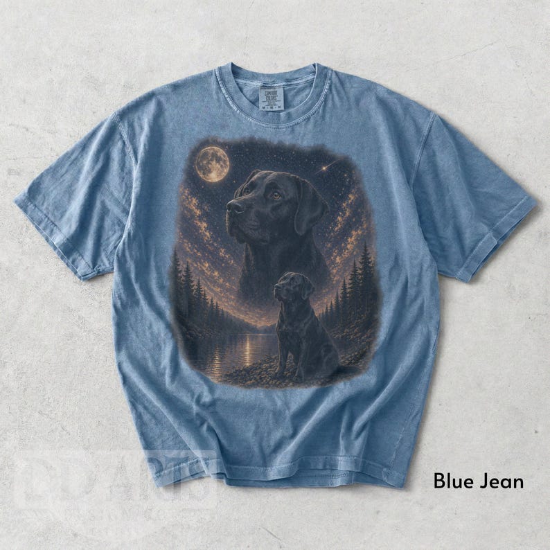 Puede incluir: Camiseta azul vaquero con una ilustraci&oacute;n detallada de un Labrador Retriever negro. La obra de arte incluye un cielo nocturno con luna llena, un lago y pinos. El texto "Blue Jean" est&aacute; impreso en la parte inferior.