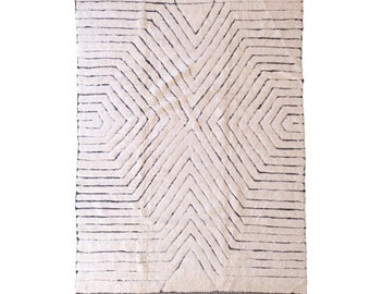 May include: A white rug with a geometric pattern in black. The pattern is made up of lines that create a starburst design.