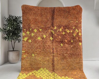 May include: A brown and yellow Moroccan rug with a geometric pattern. The rug has a fringe border and is made of wool.