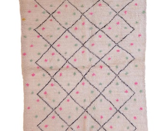 May include: A white Moroccan rug with a diamond pattern in black, pink, and green. The rug has a fringe border.