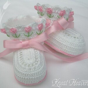 May include: A pair of white crocheted baby booties with pink satin ribbon ties and pink embroidered flowers.