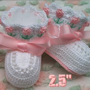 May include: White crocheted baby booties with pink satin ribbon and embroidered pink flowers. The booties are 2.5 inches long.
