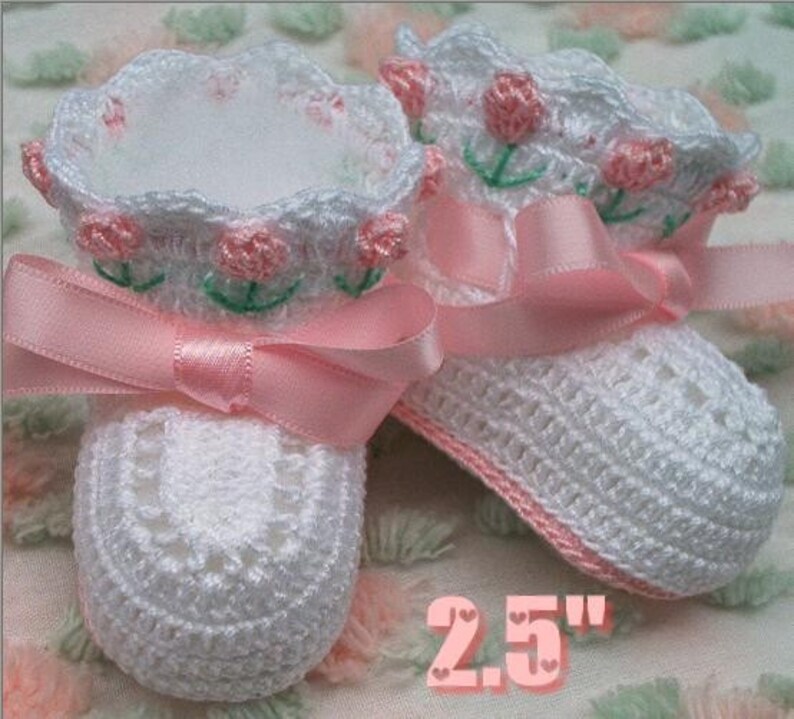 May include: White crocheted baby booties with pink satin ribbon and embroidered pink flowers. The booties are 2.5 inches long.