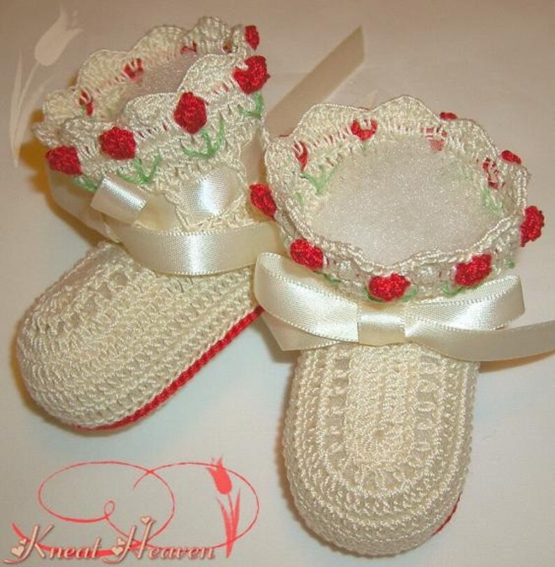 May include: A pair of crocheted baby booties with red flower accents and white satin ribbon bows.