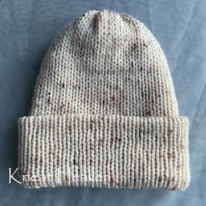 May include: A cream-colored knitted beanie with a flecked texture. The beanie has a fold-over cuff.