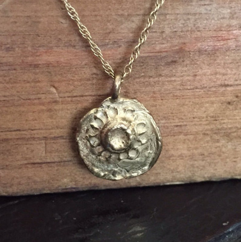 May include: A gold necklace with a round pendant featuring a raised sun design.