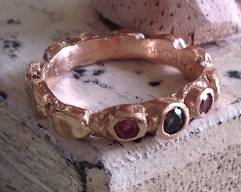 May include: A gold ring with a textured band and five gemstones. The gemstones are red, black, and clear. The ring is marked "HILLARY" on the inside.