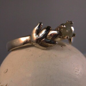 May include: A silver ring with a delicate design featuring a single, round, light green gemstone.