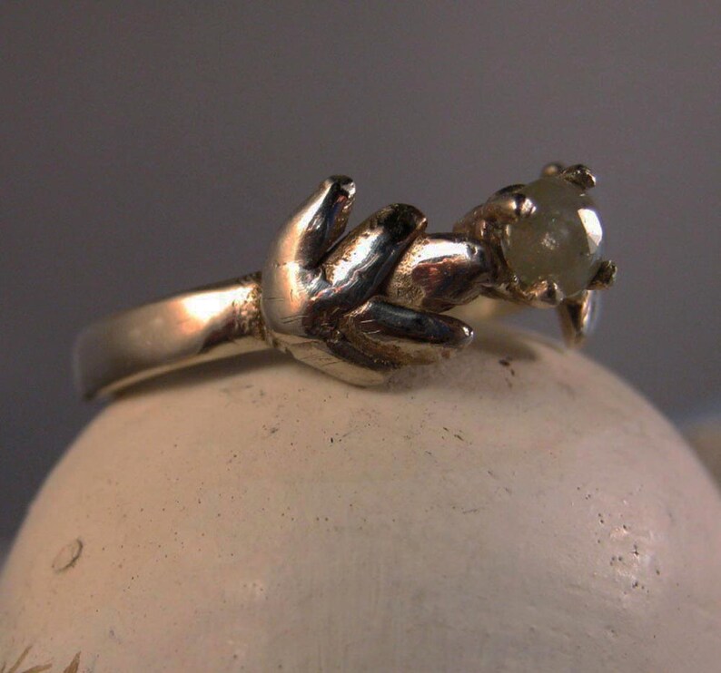 May include: A silver ring with a delicate design featuring a single, round, light green gemstone.