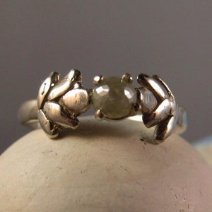 May include: A silver ring with a grey diamond set in the center, flanked by two leaf-shaped designs.