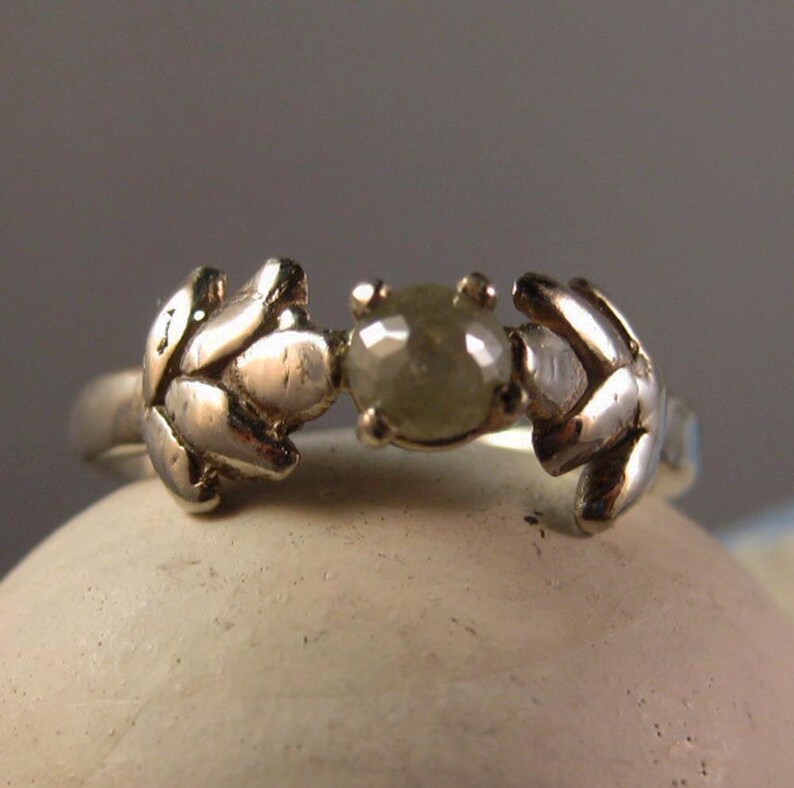 May include: A silver ring with a grey diamond set in the center, flanked by two leaf-shaped designs.