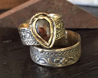 May include: Two gold rings with intricate floral designs. The top ring features a pear-shaped brown gemstone.