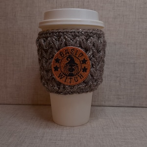 May include: A gray crocheted coffee cup cozy with a brown patch that says "Basic Witch" with a witch silhouette and stars.