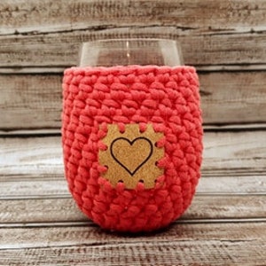 May include: A pink crocheted wine glass cozy with a heart-shaped cork detail.