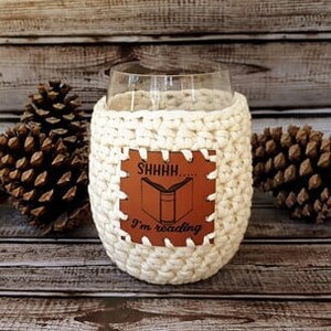 May include: White crocheted wine glass cozy with a brown leather patch that says "Shhh... I'm reading".