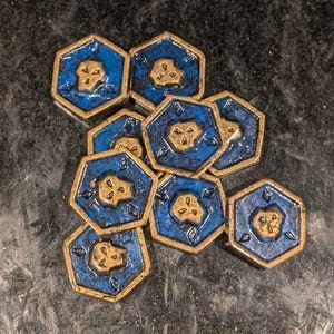 May include: A group of eight hexagonal game pieces with a blue background and gold accents. Each piece features a stylized floral design.