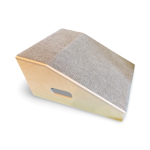 May include: Angled cat scratcher with a light wood frame and a gray carpeted scratching surface. The design features a handle cutout on the side for easy movement. The angled surface provides a comfortable scratching and lounging spot for cats.