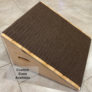 May include: Wooden pet ramp with a brown carpet top. The ramp is angled and has a small handle cut out on the side. The text "Custom Sizes Available" is printed on a white label.