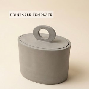 Puede incluir: Un recipiente gris de forma ovalada con tapa y asa circular. El recipiente tiene un acabado liso y mate. El texto "PRINTABLE TEMPLATE" se muestra en un rectángulo blanco encima del recipiente.