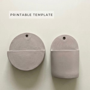 Puede incluir: Dos maceteros de pared de cerámica gris claro. Uno es circular, el otro es rectangular con la parte superior redondeada. Ambos tienen un pequeño agujero en la parte superior para colgar y una repisa en la parte inferior. El texto "PRINTABLE TEMPLATE" está en la parte superior.