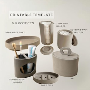 May include: A set of six grey bathroom accessories including an organiser tray, a cotton pad holder, a cotton swap holder, a toothbrush holder with a toothbrush and toothpaste, a soap dish, and a jar with a lid, labelled as a printable template.