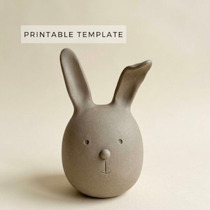 Könnte beinhalten: Eine graue Keramik-Hasenfigur mit rundem Körper und langen Ohren. Der Hase hat ein einfaches Gesicht mit zwei kleinen Augen, einer runden Nase und einem lächelnden Mund. Der Text "PRINTABLE TEMPLATE" befindet sich über dem Hasen.