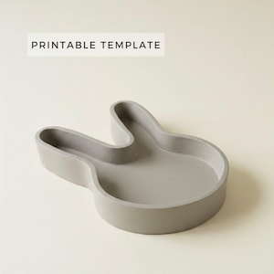 May include: A gray concrete tray in the shape of a hand with the text "PRINTABLE TEMPLATE" in a white rectangle. The tray has a rounded shape and is on a light beige background.