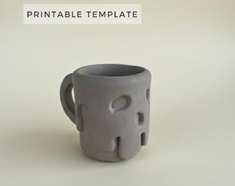 May include: A gray mug with a handle and a sculpted, abstract face design featuring recessed eye and mouth shapes. The text PRINTABLE TEMPLATE is displayed above the mug. The object has a matte finish and a rounded, organic form.