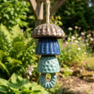 Peut inclure: Un carillon &eacute;olien en c&eacute;ramique suspendu compos&eacute; de quatre pi&egrave;ces empil&eacute;es en forme de cloche dans des tons vari&eacute;s de brun, bleu fonc&eacute; et turquoise clair. Les pi&egrave;ces pr&eacute;sentent des surfaces textur&eacute;es et sont suspendues par une corde en jute.