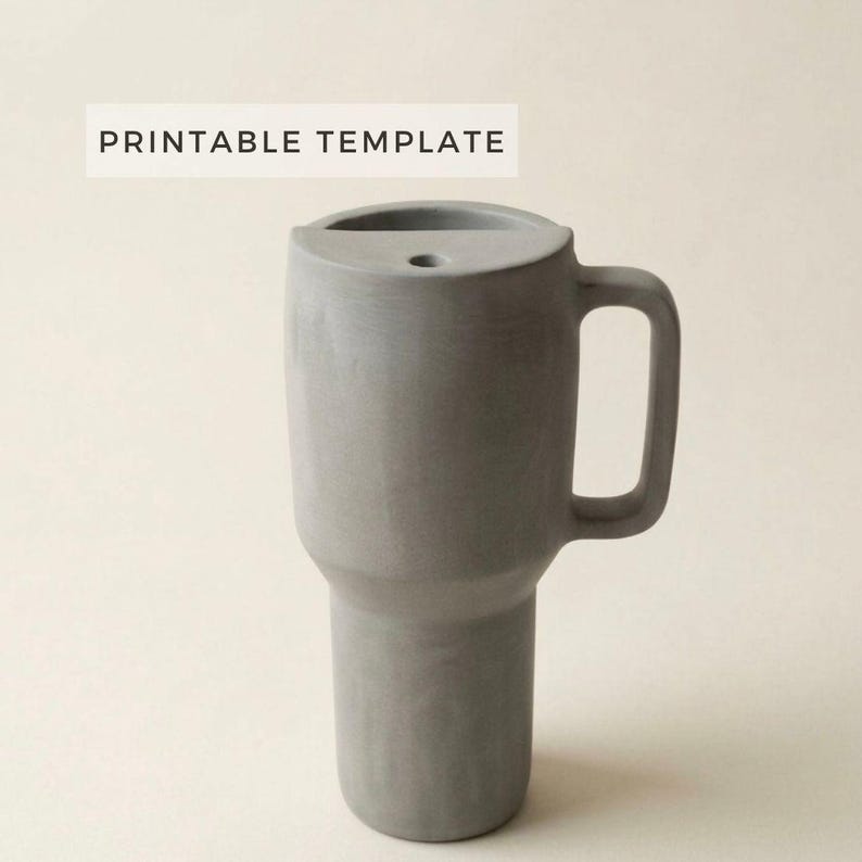 以下が含まれることがあります： ハンドルと上部に小さな穴が付いた、グレーの円筒形のタンブラー。「PRINTABLE TEMPLATE」の文字がタンブラー上部の白い長方形に印刷されています。タンブラーは、滑らかな素材でできています。
