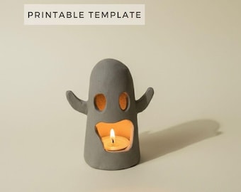May include: A gray ghost-shaped tea light candle holder with two oval eye cutouts and a large mouth opening. A lit tea light candle is visible inside the hollow center. The text PRINTABLE TEMPLATE is displayed above the object.