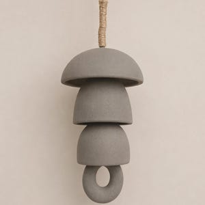 Peut inclure: Un carillon suspendu compos&eacute; d'&eacute;l&eacute;ments en c&eacute;ramique gris mat. La structure comprend un sommet en forme de d&ocirc;me large, deux pi&egrave;ces plus petites en forme de bol et un anneau circulaire &agrave; la base, le tout suspendu par une corde de jute &eacute;paisse.