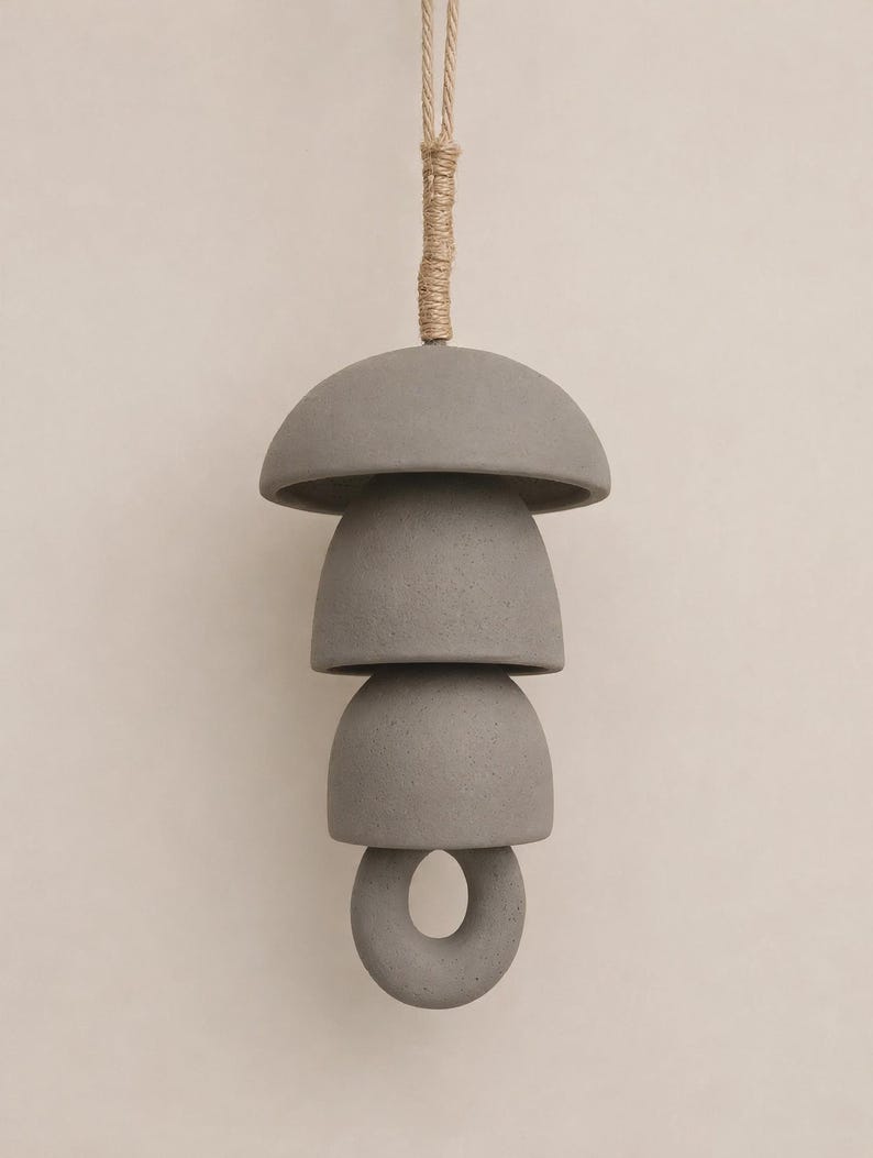 Peut inclure: Un carillon suspendu compos&eacute; d'&eacute;l&eacute;ments en c&eacute;ramique gris mat. La structure comprend un sommet en forme de d&ocirc;me large, deux pi&egrave;ces plus petites en forme de bol et un anneau circulaire &agrave; la base, le tout suspendu par une corde de jute &eacute;paisse.