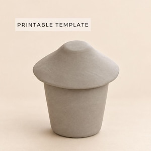 May include: A matte gray, mushroom-shaped container with a wide, rounded lid and a tapered base. The text PRINTABLE TEMPLATE is displayed in a rectangular box above the object, which has a smooth, solid-colored surface texture.