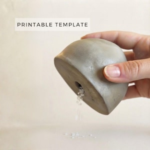 Può includere: Una saliera in cemento grigio a forma di cupola con un'apertura circolare alla base, da cui fuoriescono piccoli cristalli di sale bianchi. L'immagine include il testo PRINTABLE TEMPLATE nell'angolo in alto a sinistra su sfondo neutro.