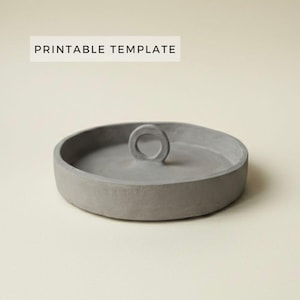 Puede incluir: Una bandeja de hormigón gris con un asa circular. La bandeja es redonda, de perfil bajo y con una superficie lisa. El texto "PRINTABLE TEMPLATE" está en un rectángulo blanco encima de la bandeja.