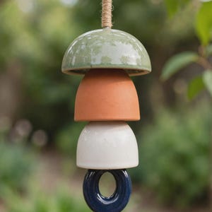 Peut inclure: Un carillon &eacute;olien en c&eacute;ramique suspendu par une corde de jute, compos&eacute; de quatre &eacute;l&eacute;ments empil&eacute;s. La pi&egrave;ce sup&eacute;rieure est un d&ocirc;me vert sauge brillant, suivi d'un bol en terre cuite mat, d'un bol cr&egrave;me brillant et d'un anneau bleu marine.