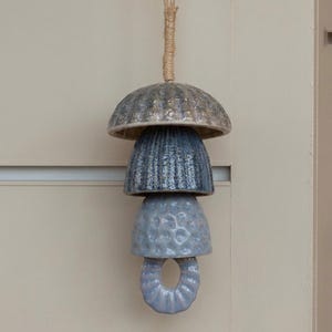 Peut inclure: Un carillon &eacute;olien en c&eacute;ramique suspendu compos&eacute; de quatre &eacute;l&eacute;ments empil&eacute;s dans des tons de bleu et de gris. La pi&egrave;ce sup&eacute;rieure est un d&ocirc;me large et textur&eacute;, suivi de deux composants en forme de cloche avec des surfaces nervur&eacute;es.