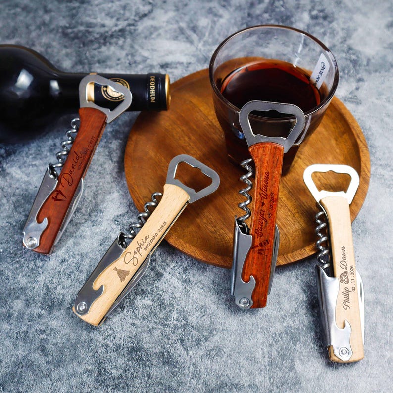 May include: Four stainless steel waiter's corkscrews with wooden handles, each featuring custom laser-engraved names and dates. The corkscrews include a bottle opener, a foil cutter, and a spiral worm, displayed alongside a glass of red wine.