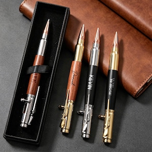 Könnte beinhalten: Eine Sammlung von kugelförmigen Stiften in verschiedenen Farben und Ausführungen. Ein Stift befindet sich in einer schwarzen Box. Die Stifte haben goldene, silberne und Holz-Akzente. Die Stifte sind mit Namen graviert. Der Hintergrund umfasst eine braune Lederbrieftasche.