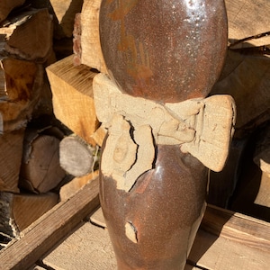 Peut inclure: Une grande sculpture en céramique émaillée brun foncé avec une surface lisse et réfléchissante. Elle présente une bande d'argile texturée de couleur claire enroulée autour du milieu, rappelant un nœud, avec des bords bruts façonnés à la main.