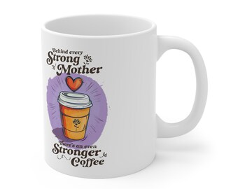 May include: White ceramic coffee mug with a purple and white illustration of a coffee cup with a heart above it. The text reads "Behind every strong mother there's an even stronger coffee."