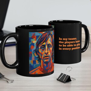 Puede incluir: Dos tazas de café negras. Una taza presenta un retrato colorido de una persona. La otra taza tiene el texto: "En mis equipos, los jugadores tienen que poder jugar en todas las posiciones". Las tazas están sobre una superficie clara.
