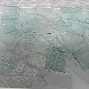 以下が含まれることがあります： 透明な長方形のガラス片のコレクション。一部はテクスチャ加工された表面を持ち、白い容器内の白い液体に浸かっています。 ガラスの破片はサイズと形状が異なり、散らばった配置になっています。