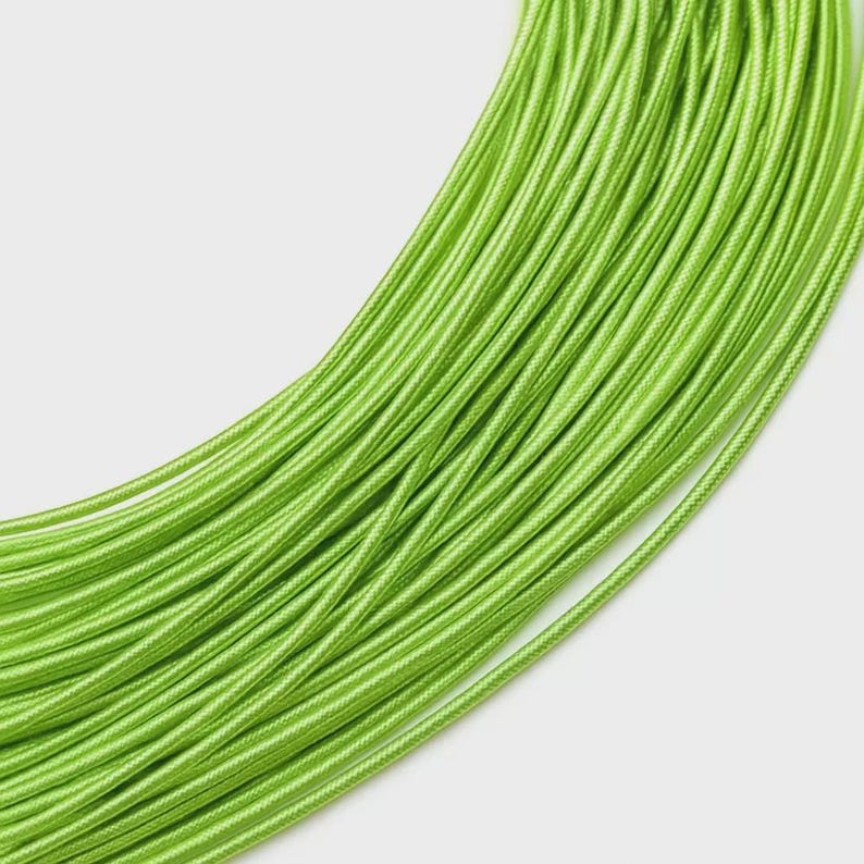 May include: A coiled length of bright lime green fabric cord featuring a tightly woven, smooth, and uniform texture. The cord is arranged in a series of concentric, overlapping loops that create a continuous, flowing pattern of parallel lines.