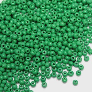 May include: A close-up shot of a pile of small, round, bright green beads. The beads are densely packed together, filling the frame. Each bead has a hole running through the center. The beads are likely used for jewelry making or crafting.