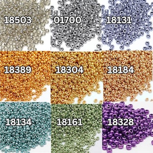 Puede incluir: Una colección de pequeñas cuentas redondas en varios colores, incluyendo plata, oro, turquesa y morado. Cada montón de cuentas tiene un código de producto único impreso, como "18503" y "01700". Estas cuentas probablemente se utilizan para hacer joyas u otras manualidades.