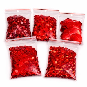 May include: Five clear plastic bags filled with red sequins. The sequins are round and shiny, and the bags are sealed with a red zip. The bags are arranged in a slightly offset pattern against a white background.