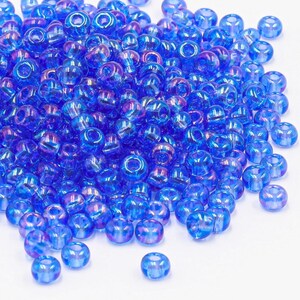 Könnte beinhalten: Ein Haufen kleiner, irisierender blauer Glasperlen. Die Perlen sind rund und haben ein Loch in der Mitte. Sie sind perfekt für die Schmuckherstellung oder andere Bastelprojekte.