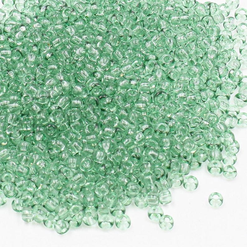 May include: A large pile of small, light green glass seed beads. The beads are round and have a slightly iridescent finish.